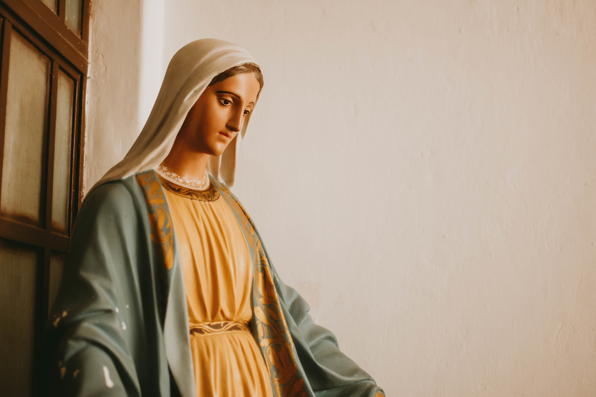 Closeup shot of a Mary, mother of Jesus statue against a white wall